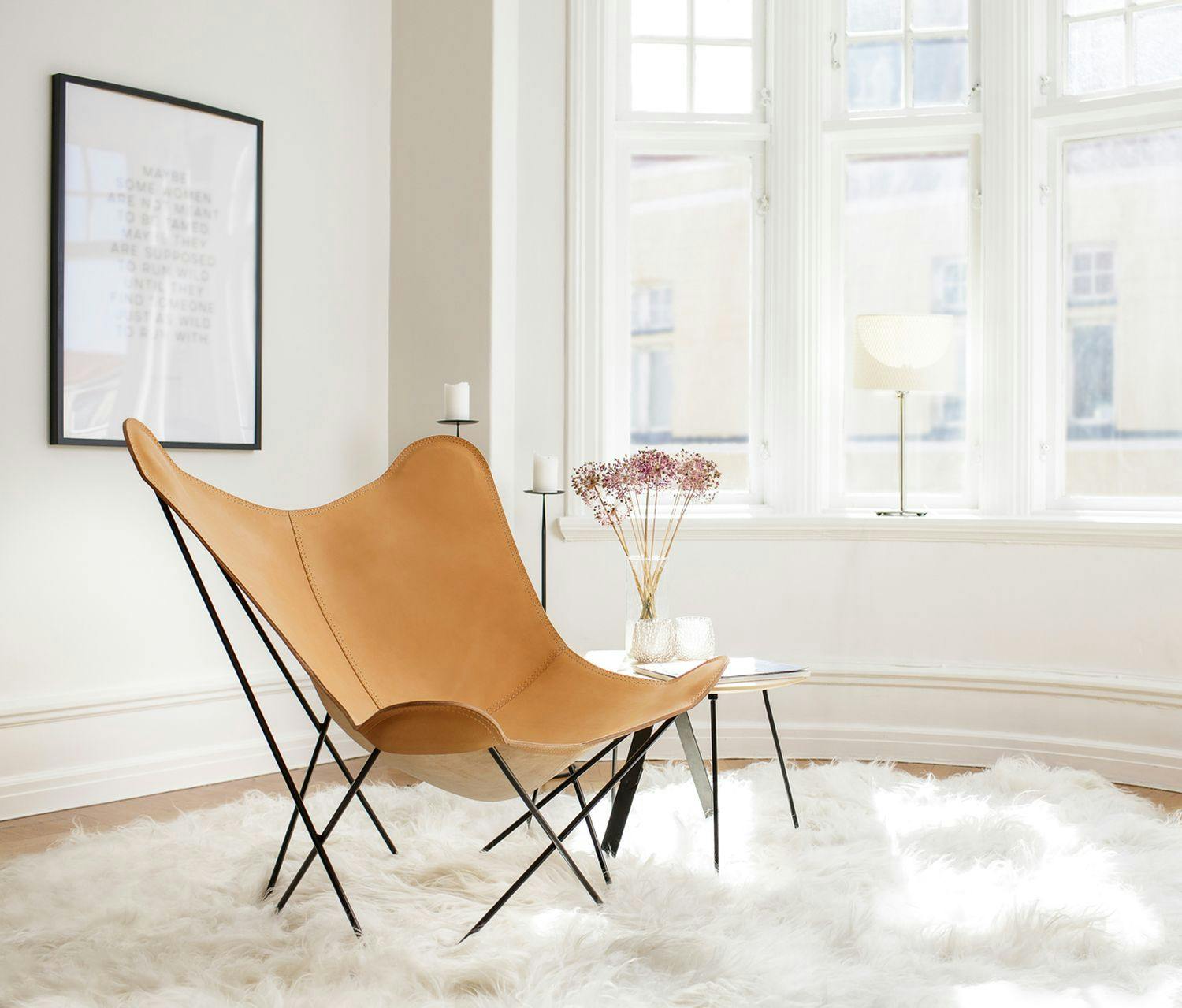 Cadeira borboleta de couro natural em uma sala de estar com uma pele de ovelha por baixo.