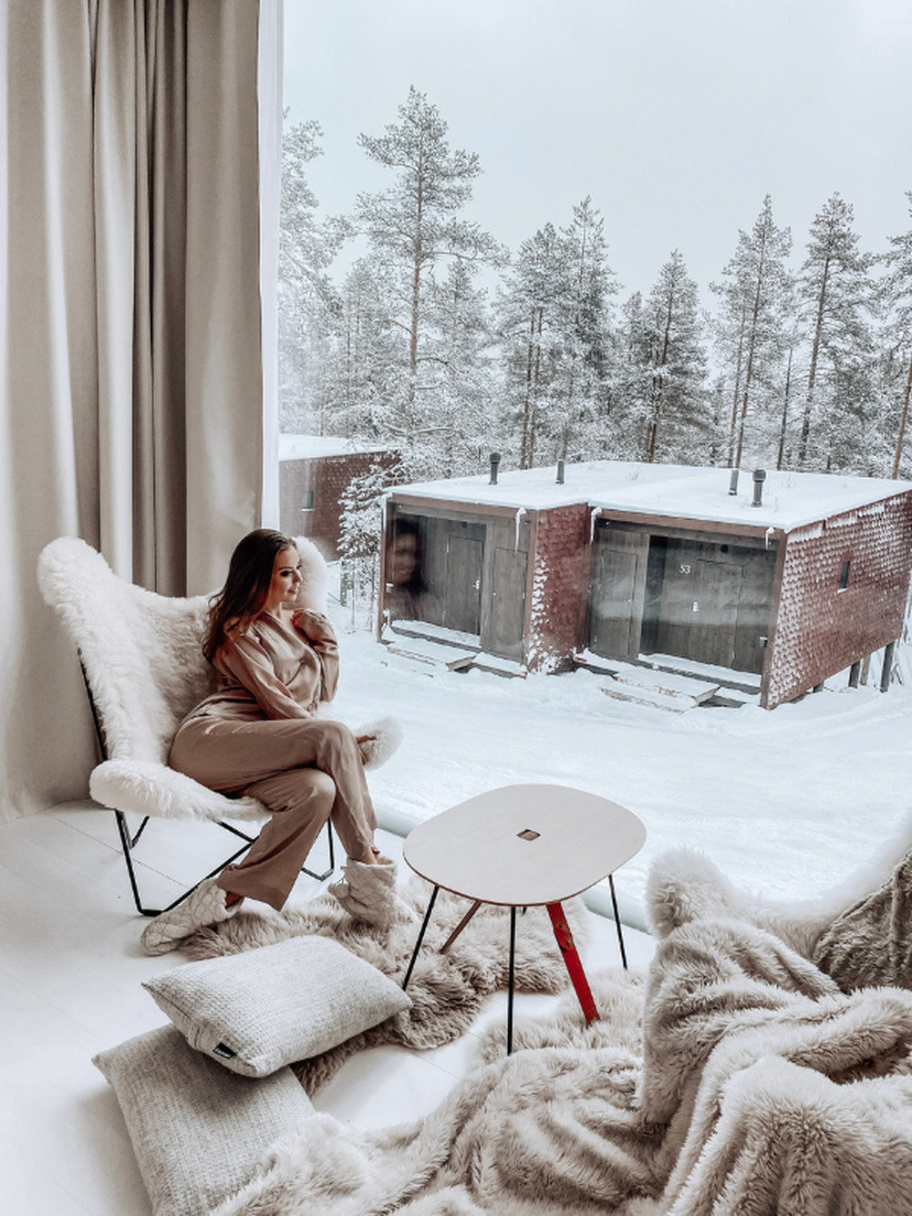 Eine Frau, die in einem Schaffell Schmetterlingsstuhl in einer luxuriösen Hütte im Winter sitzt.