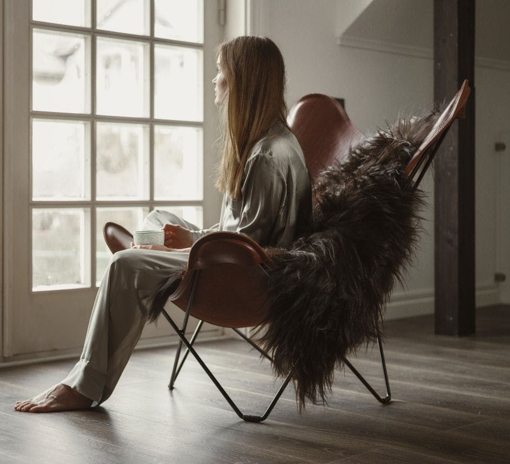Frau sitzt in einem Lederschmetterlingsstuhl mit schwarzem Schaffell-Überwurf